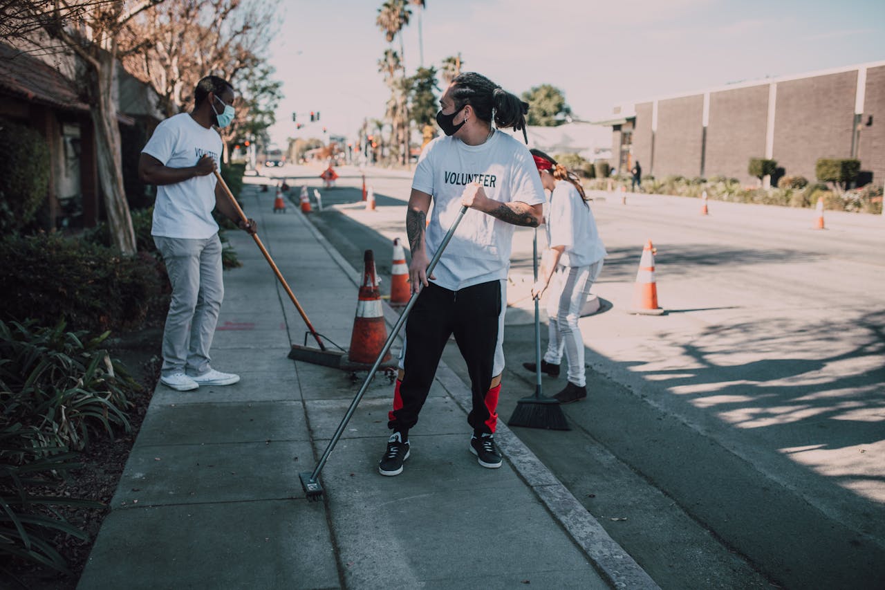 Volunteers wearing masks sweep an urban sidewalk, enhancing community and social good efforts.